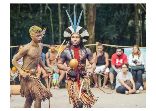 Foto van twee Pataxó in traditionele kleding tijdens een voorstelling voor een groep toeschouwers.