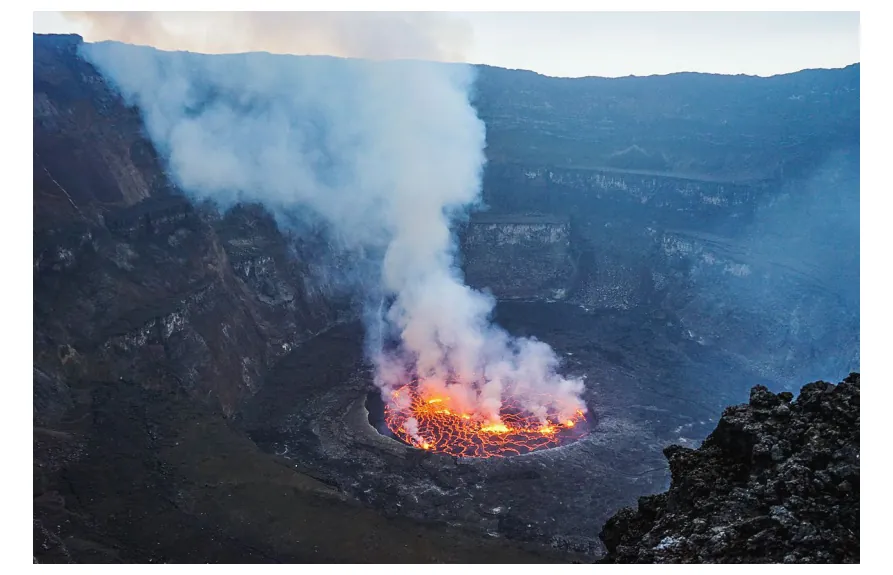 Foto van de krater van de Nyiragongo met een borrelend lavameer en opstijgende rookpluimen.