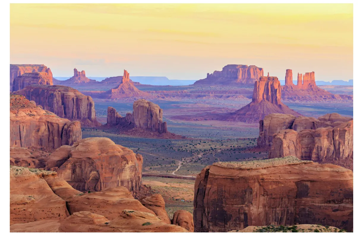 Foto van de rotsformaties van Monument Valley bij zonsondergang, met rode zandstenen torens en een vlakte op de achtergrond.