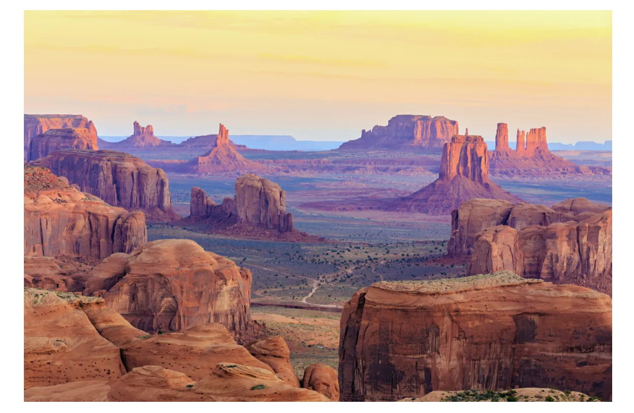 Rotsformaties van Monument Valley bij zonsopgang, met roodbruine zandsteen en een vlakte op de achtergrond.
