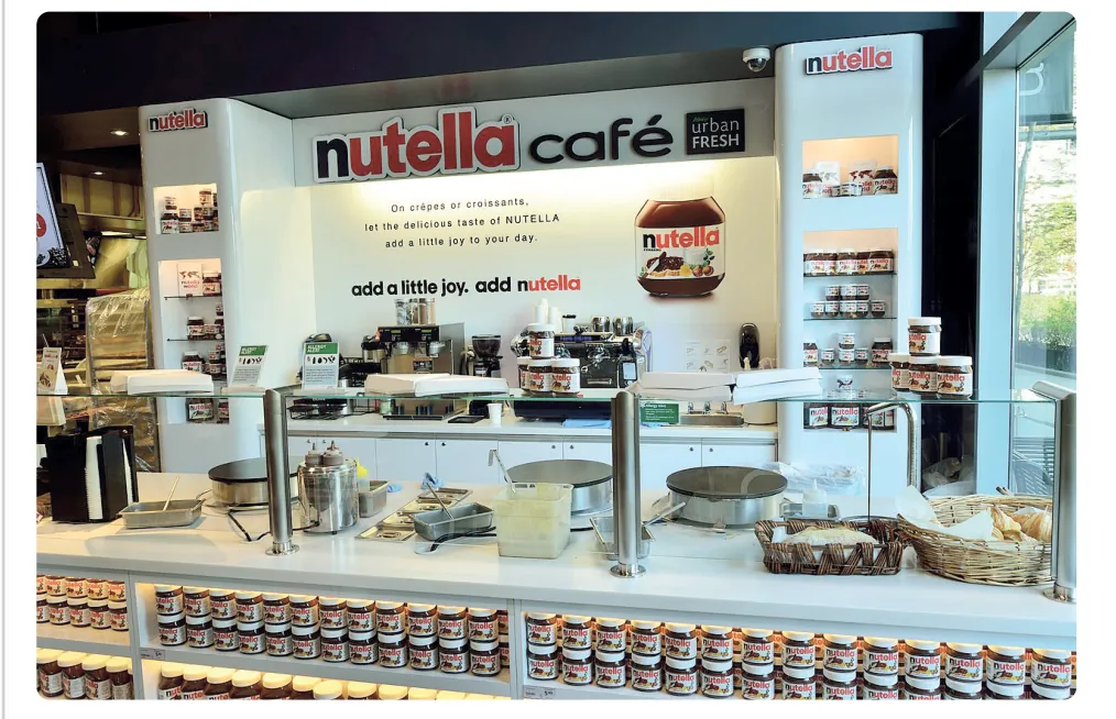 Foto van een Nutella-café met een toonbank vol crêpes en croissants en rijen potten Nutella in de vitrine.