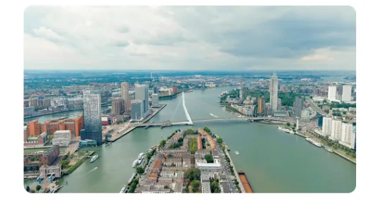 Luchtfoto van een stad met hoge gebouwen aan een brede rivier, met een brug over het water.