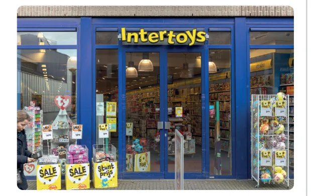 Winkelpui van een Intertoys-winkel met blauwe gevel, met speelgoed en sale-borden voor de ingang.