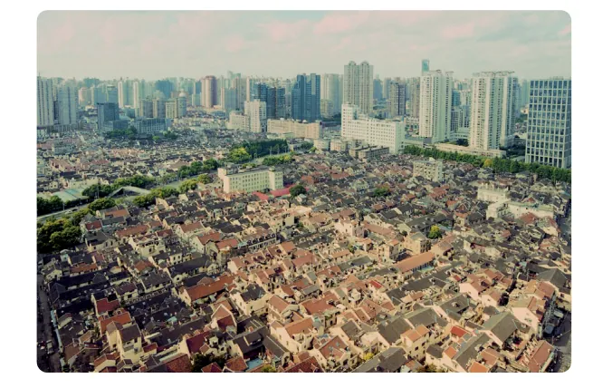 Foto van een dicht bebouwde wijk met oude lage daken op de voorgrond en hoge flats en kantoortorens op de achtergrond.