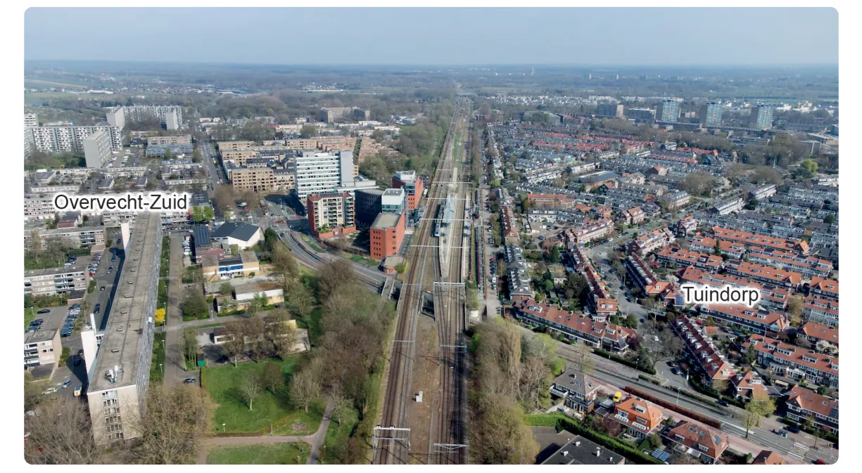 Luchtfoto van een spoorlijn die de grens vormt tussen Overvecht-Zuid met hoge flats en kantoorgebouwen aan de linkerkant en Tuindorp met rijtjeshuizen met rode daken en tuinen aan de rechterkant.