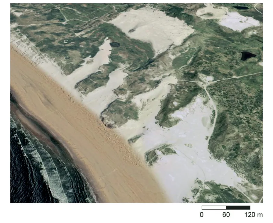 Luchtfoto van dezelfde duinen in 2023, met de vijf windsleuven in het duinlandschap en het strand langs de kust, met een schaal van 120 meter.
