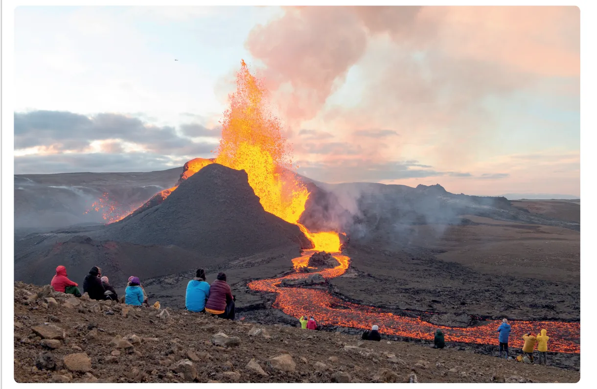 Foto van een lavafontein en een lavastroom bij een nieuwe vulkaan, met een groep toeristen die op korte afstand toekijkt.