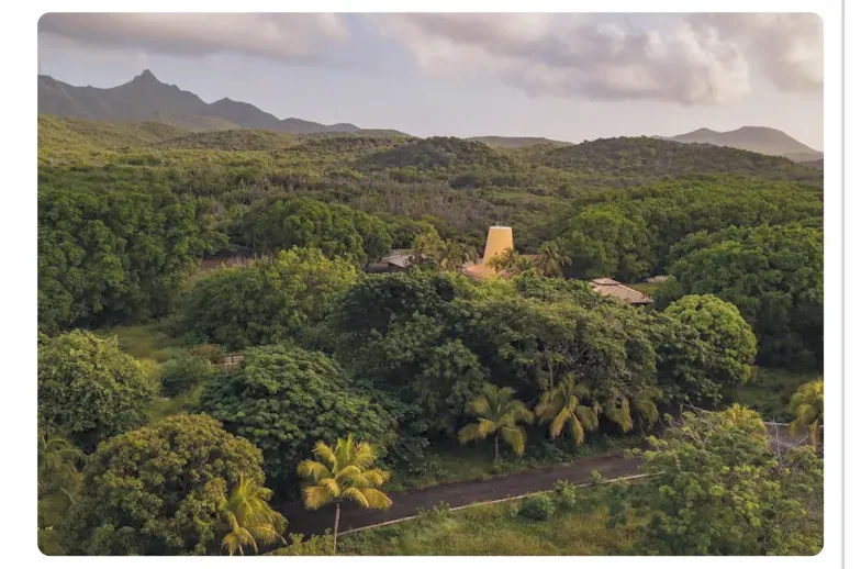 Luchtfoto van het natuurpark Hòfi Mango met veel groene bomen, een oud gebouw met toren en palmen.