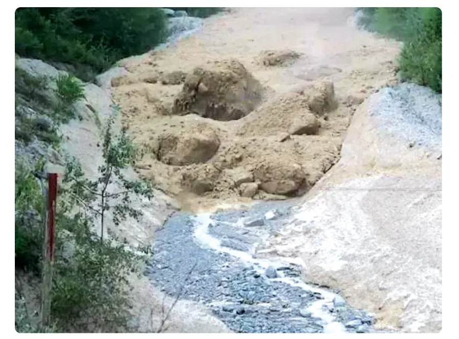 Foto van een modderstroom: lichtbruin modder met grote brokken materiaal en een grijze stroom water aan de voet van een helling.