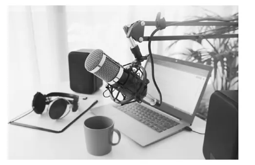Foto van een microfoon, koptelefoon en laptop op een bureau, opgesteld voor een podcast.