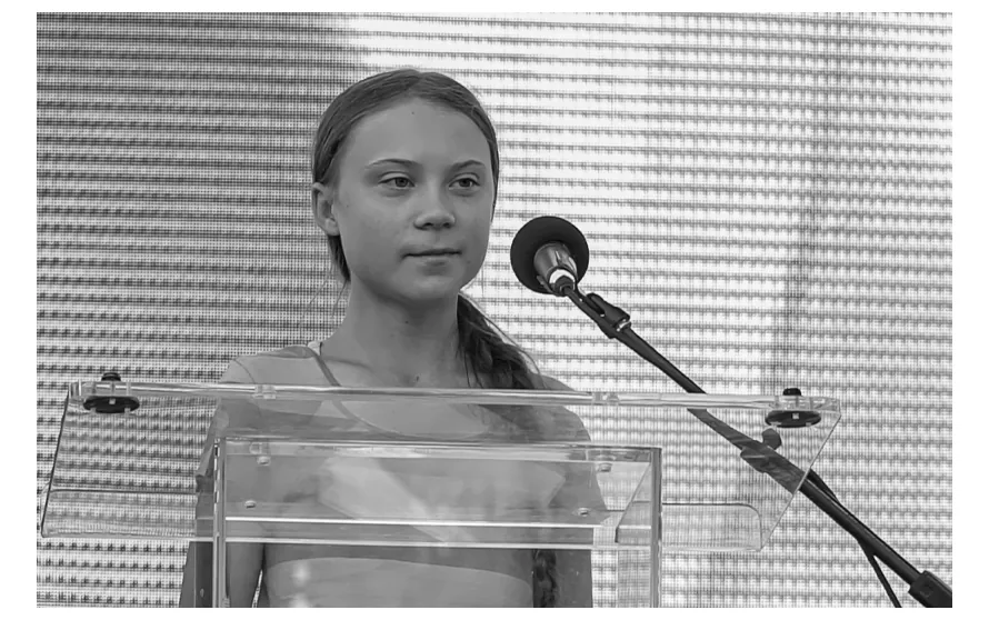 Foto van Greta Thunberg die achter een doorzichtig spreekgestoelte staat, met een microfoon voor zich.