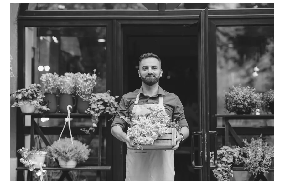 Foto van een bloemist met een kistje planten voor zijn winkel.