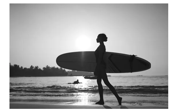 Silhouet van een surfer met een surfplank op het strand.