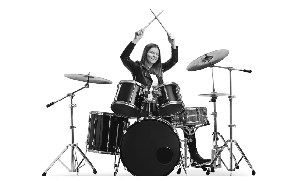 Foto van een jonge vrouw die achter een drumstel zit, met de drumstokken in de lucht.