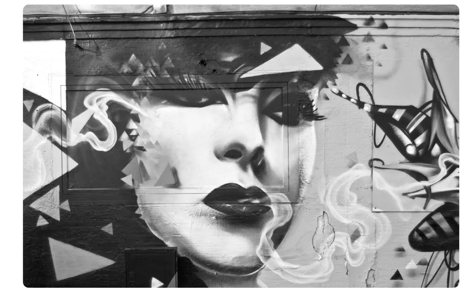 Zwart-witte graffitimuurschildering van een vrouwengezicht met rook en geometrische vormen eromheen.