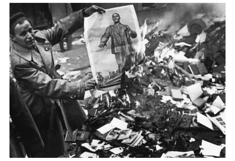 Foto van een man die een portret van Lenin boven een brandende stapel papier houdt.