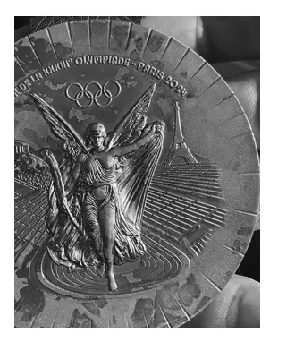 Zwart-witfoto van een bronzen medaille van de Olympische Spelen van Parijs 2024 met vlekken en verkleuringen op het oppervlak.
