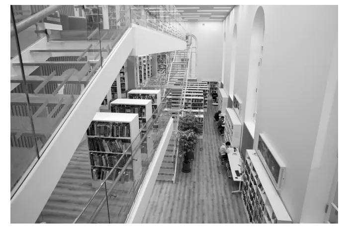 Foto van een lichte bibliotheek met een glazen loopbrug, boekenkasten en een trap op de verdieping.