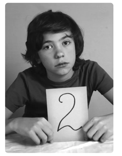 Foto van een jongen met een ontevreden blik die een kaartje met het cijfer 2 omhoog houdt.