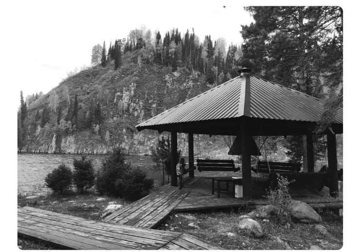 Foto van een houten paviljoen met bankjes aan de oever van een rivier, met een beboste rotswand op de achtergrond.