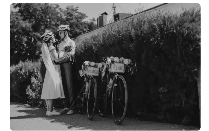 Foto van het bruidspaar met fietshelmen op, staand naast twee versierde fietsen bij een heg.