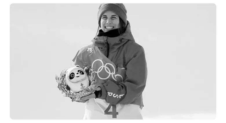 Zwart-witfoto van een glimlachende sportvrouw met muts, die een knuffelpanda in haar armen houdt.