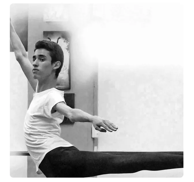 Zwart-witfoto van een jonge danser die in een balletpositie aan de barre staat.