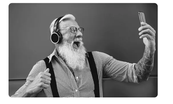 Zwart-witfoto van een oudere man met witte baard en koptelefoon die enthousiast een selfie maakt.