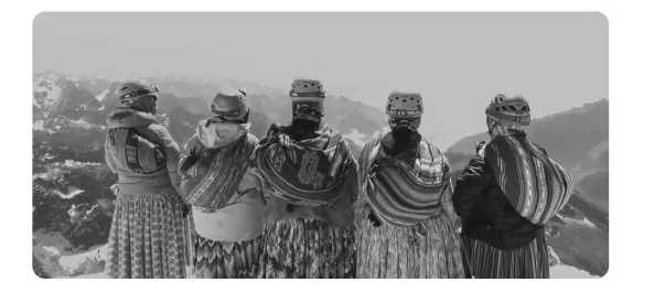 Zwart-witfoto van vijf vrouwen in traditionele kleding met helmen, op de rug gezien, met besneeuwde bergen op de achtergrond.
