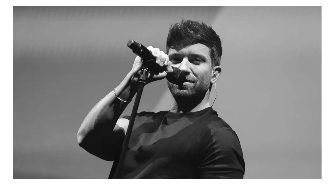 Zwart-witfoto van zanger Pablo Alborán die op een podium in een microfoon op een standaard zingt.