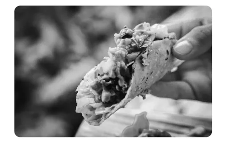 Foto van een hand die een taco vasthoudt, gevuld met groente.