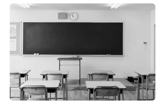 Foto van een lege klas met een schoolbord, tafels en stoelen.