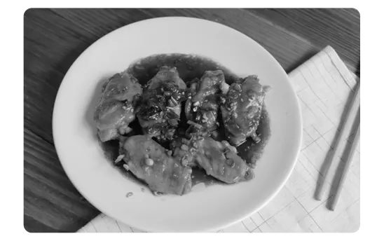 Foto van een wit bord met stukken pollo a la Coca Cola in saus, naast een servet met eetstokjes.