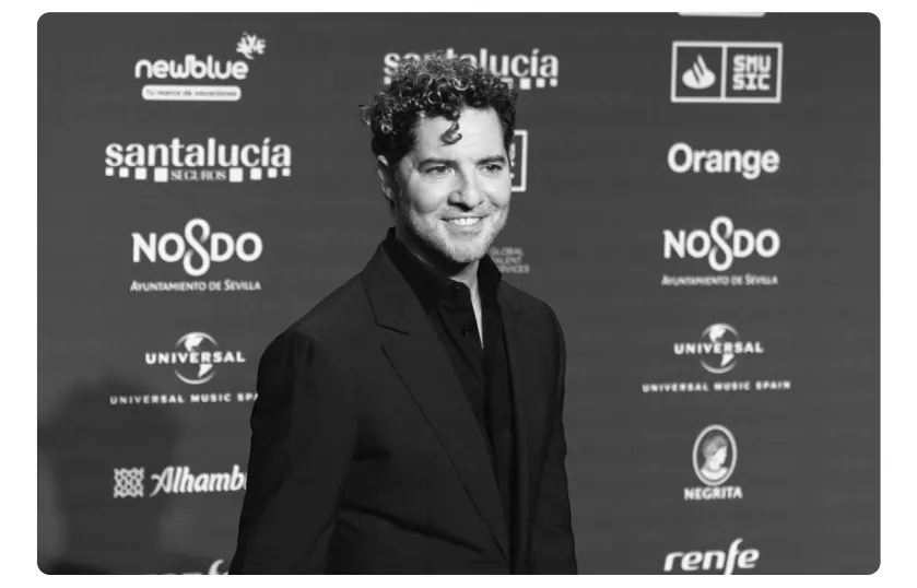 Foto van David Bisbal in een zwart pak voor een wand met logo's van sponsors.
