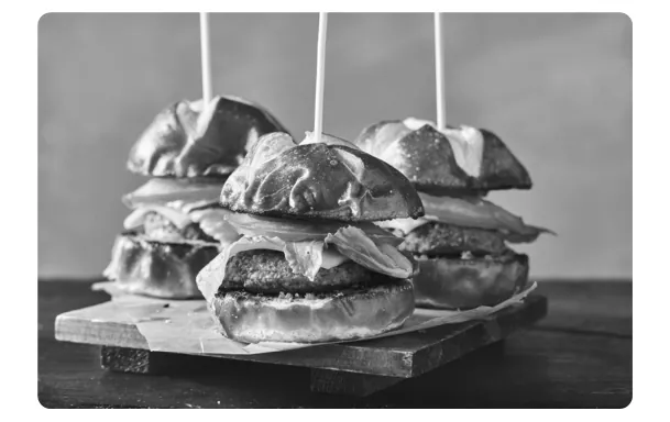 Drie mini-hamburgers op een houten plank, met stokjes erdoor.