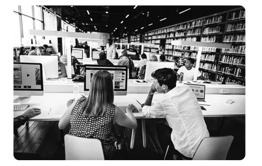 Zwart-witfoto van studenten die achter computers zitten in een bibliotheek.