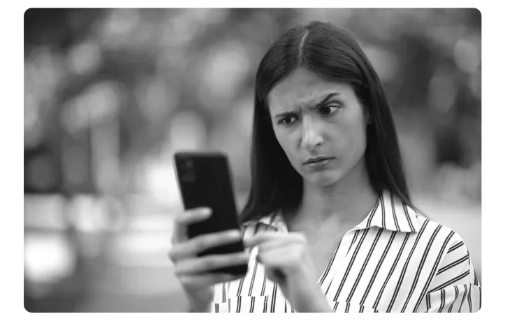 Zwart-witfoto van een vrouw die fronsend naar het scherm van haar telefoon kijkt.