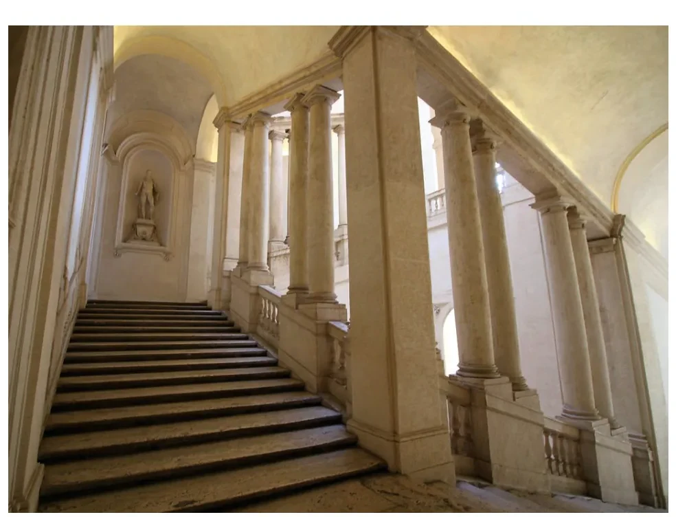 Blik omhoog door het trappenhuis van Bernini: hoge zuilen en bogen rond de trap, met doorkijkjes naar de verdiepingen en de nissen met beelden.