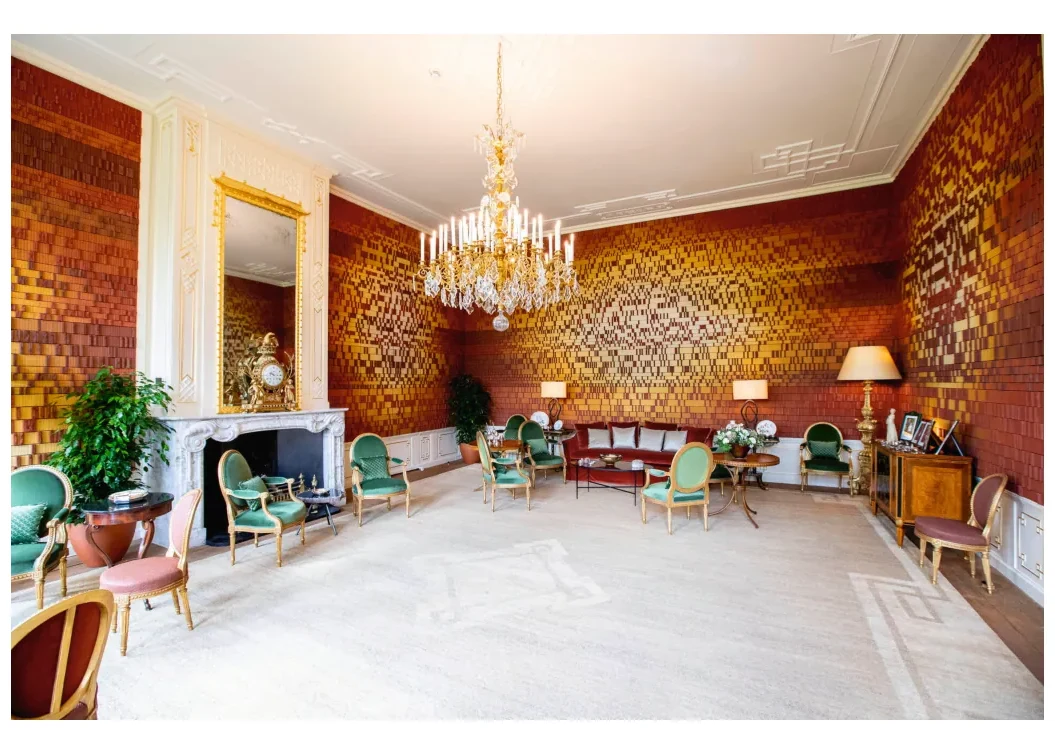 Salon met een vloer en wanden van gekleurde bakstenen, een kroonluchter, groene stoelen en een rode bank.