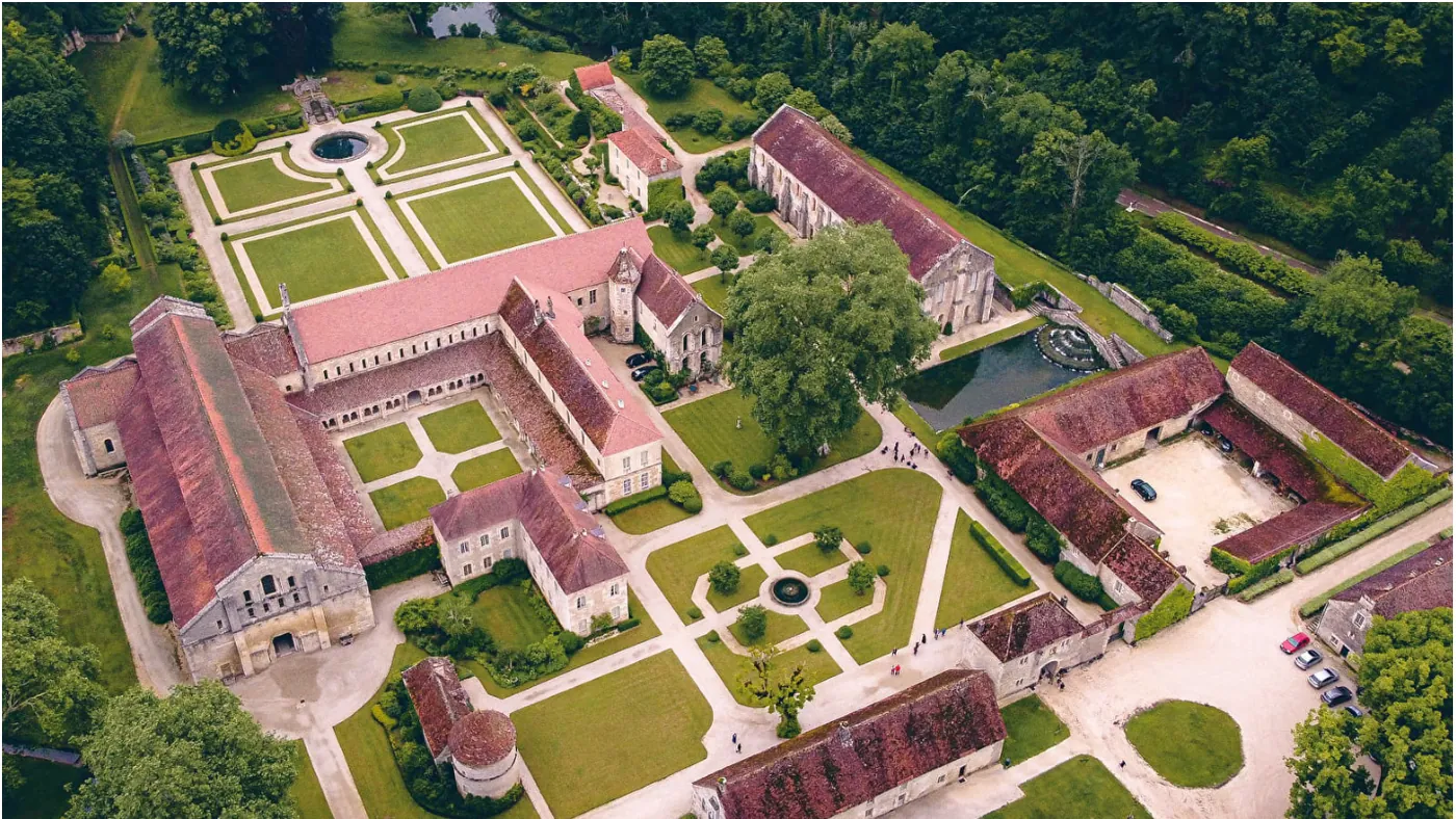 Luchtfoto van het kloostercomplex van Fontenay: links de lange kerk met roodbruin pannendak, daarnaast vleugels rond een binnenhof, tuinen met geometrische perken en bijgebouwen tussen de bomen.