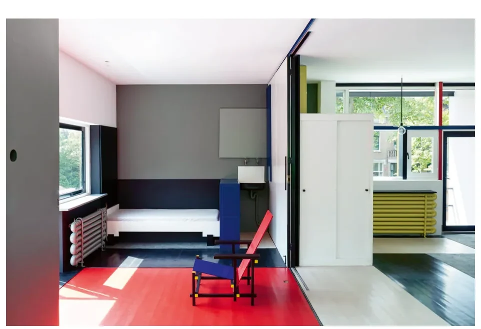 Interieur met een rode vloer, een grijze wand, een blauwe stoel en een gele radiator; links een raam met een openslaand deel.