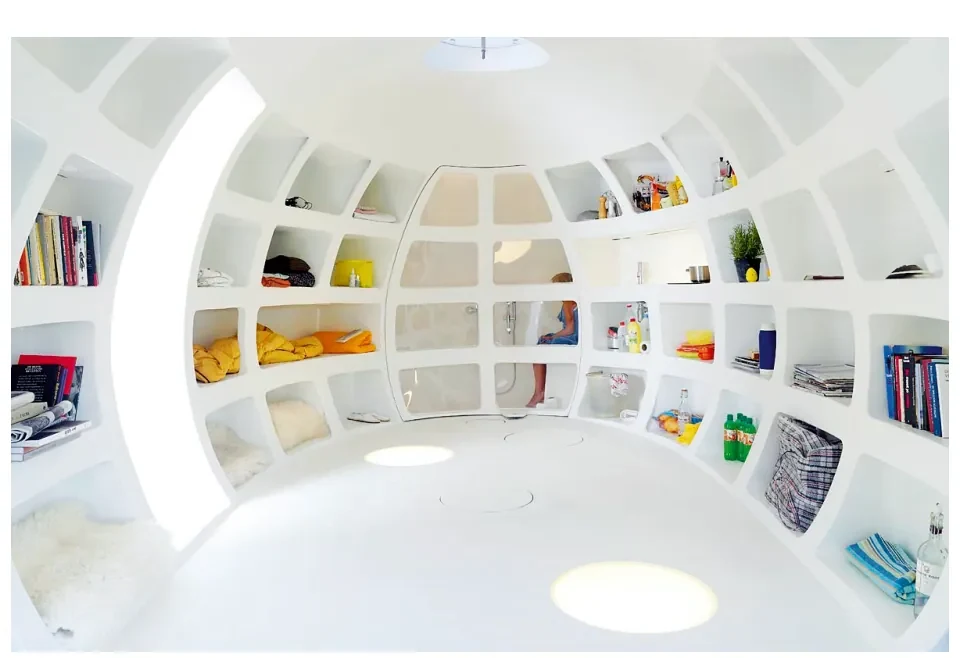 Binnenkant van een witte, ronde ruimte met gebogen, ingebouwde boekenplanken vol boeken en voorwerpen.