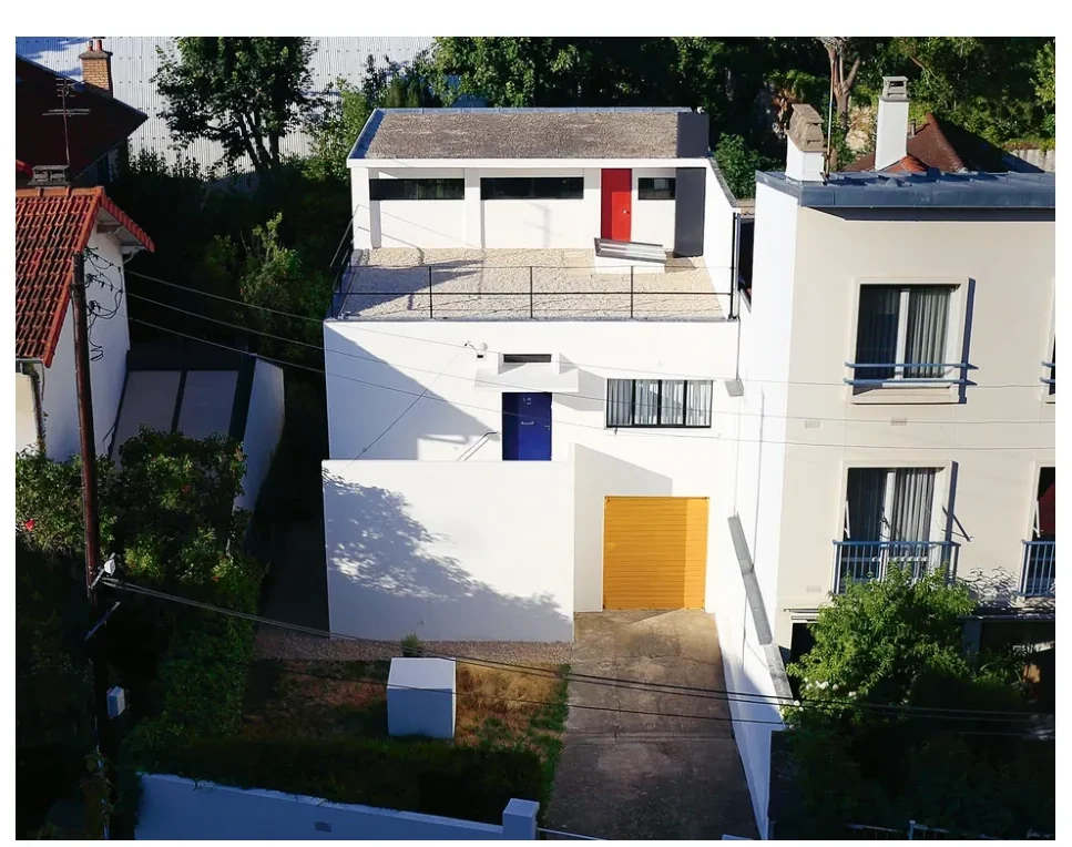 Witte, gepleisterde voorgevel van de atelierwoning met een gele, kubusvormige aanbouw, rode en blauwe accenten en grote ramen.