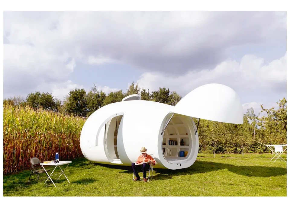 Witte, ronde woonunits in een grasveld met riet; bij een van de openingen zit een persoon aan een tafel.