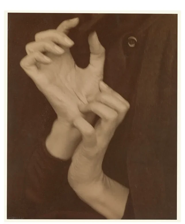 Sepia foto van een hand met gespreide, gekromde vingers tegen een donkere achtergrond.