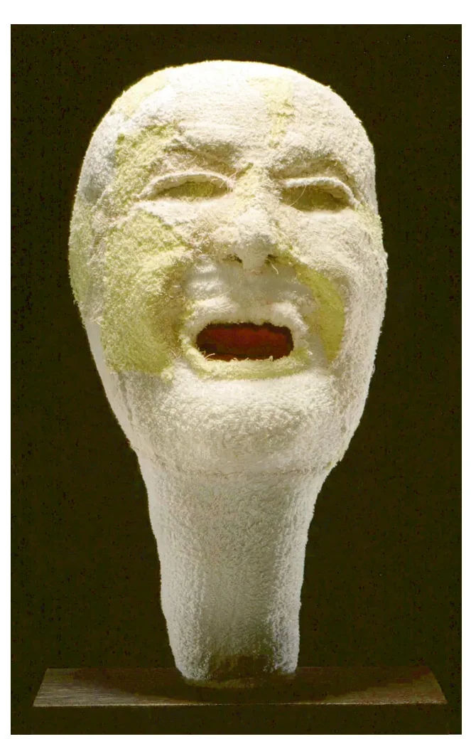 Witte, sculpturale vorm van een gezicht met een lange, uitlopende kin en een open rode mond, op een donkere achtergrond.