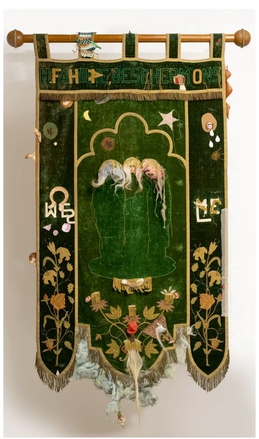 Groen vaandel met goudkleurige plantmotieven en franje; in het midden drie vrouwelijke figuren in een gewelfde vorm, met geborduurde letters aan de zijkant.