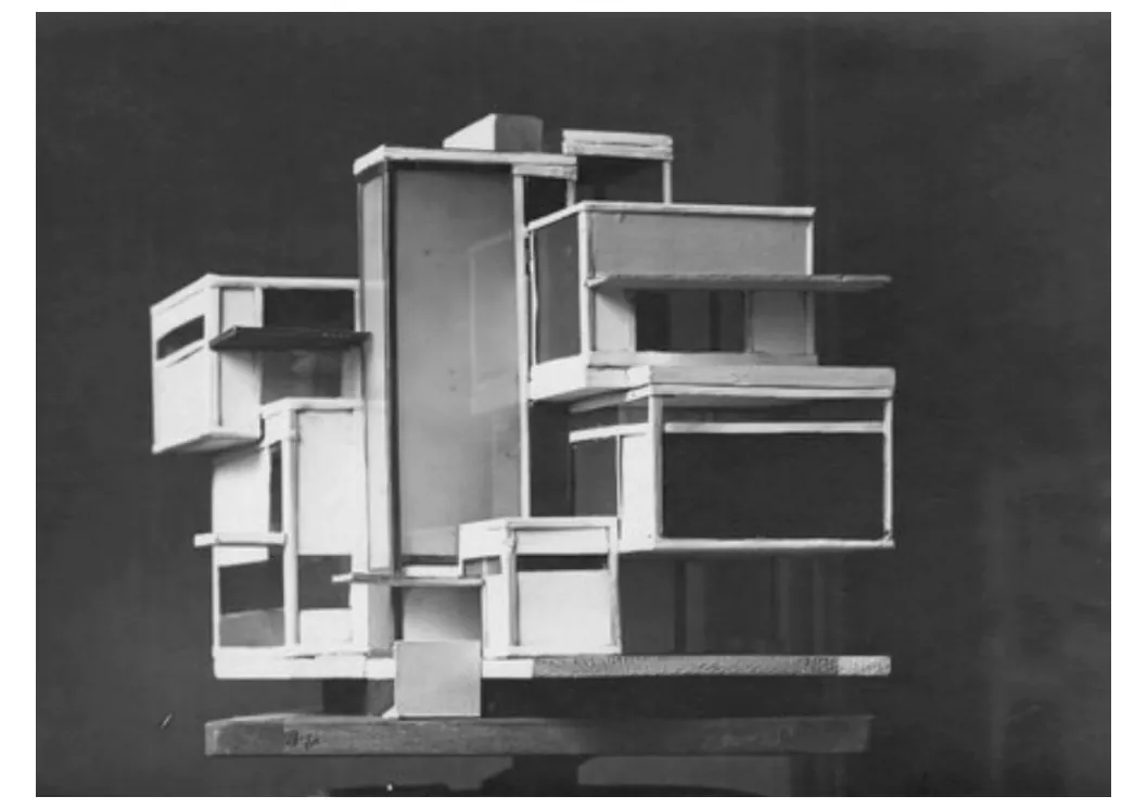 Zwart-witfoto van een maquette: witte, onregelmatig gestapelde blokken met balkons en platte vlakken, op een donkere achtergrond.