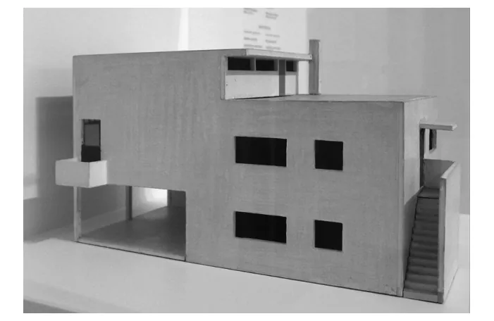 Foto van een maquette van de atelierwoning: een grijze, betonachtige gevel met grote donkere raamopeningen en een open buitentrap aan de rechterkant.