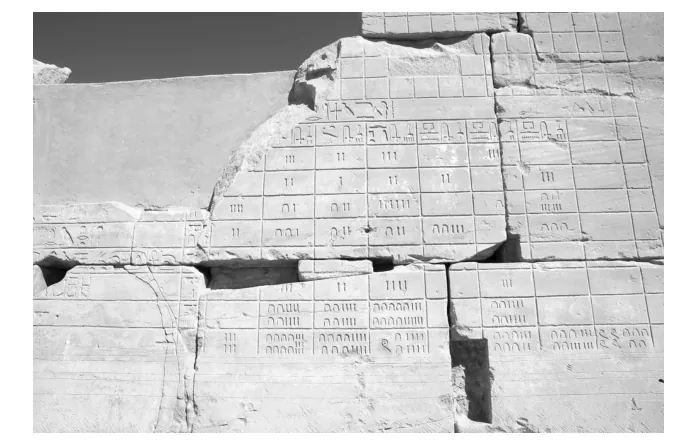 Zwart-witfoto van een verweerde stenen muur met een in rijen en vakken uitgehakte oud-Egyptische kalender met hiërogliefen.